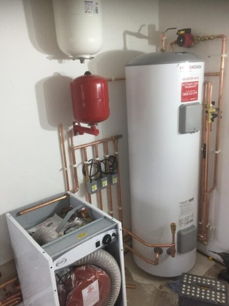An oil boiler system with a large tank, red expansion vessel, and connected pipes in a utility room.