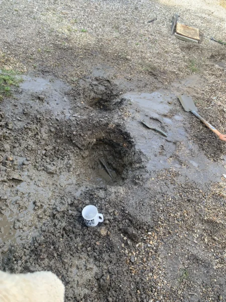 Burst alcathene water main repair excavation in North Tuddenham, Dereham, showing muddy hole with tools and mug