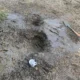 Burst alcathene water main repair excavation in North Tuddenham, Dereham, showing muddy hole with tools and mug